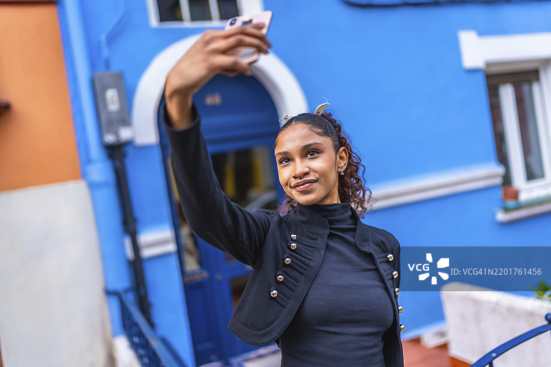 美丽的年轻非裔美国女性在城市中一栋蓝色彩色房子外自拍图片素材