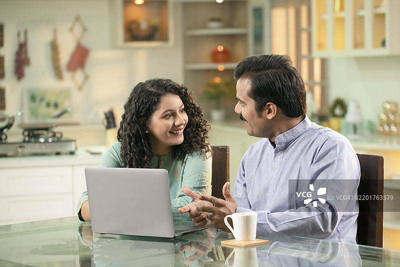 印度女性在厨房做饭，丈夫在桌子上看报纸。图片素材
