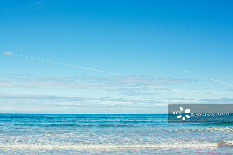 平静的蓝绿色海洋波浪在蓝天下轻轻拍打着海岸图片素材