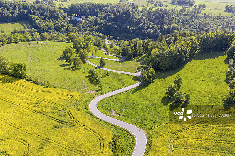 从Reifland到Rauenstein的盛开油菜花田间蜿蜒曲折的公路鸟瞰图,背景是Rauenstein城堡,位于德国萨克森州的埃尔茨山脉,波卡乌-伦根费尔德。图片素材