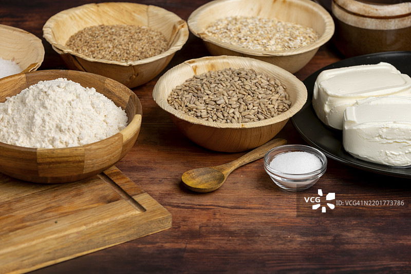 木桌上放着木碗里的烘焙原料，如面粉、干酪、盐和葵花籽。图片素材