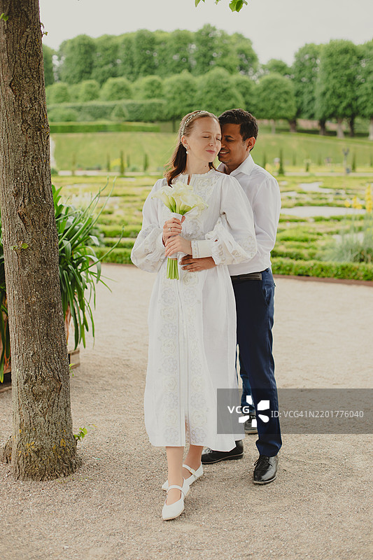 一对情侣站在人行道上，背景是树木。图片素材