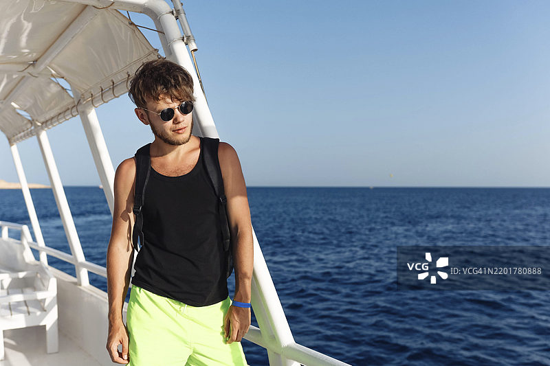 戴着太阳镜的男子站在船上，背景是阳光明媚的海洋图片素材
