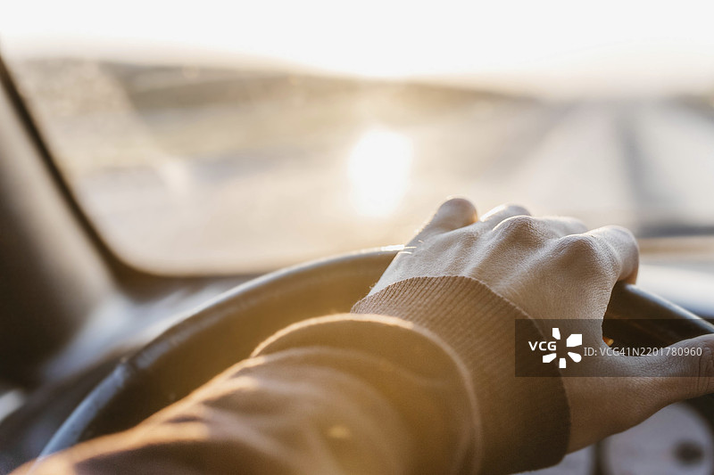 一只手握着汽车方向盘，明亮的阳光透过窗户洒进车内。图片素材
