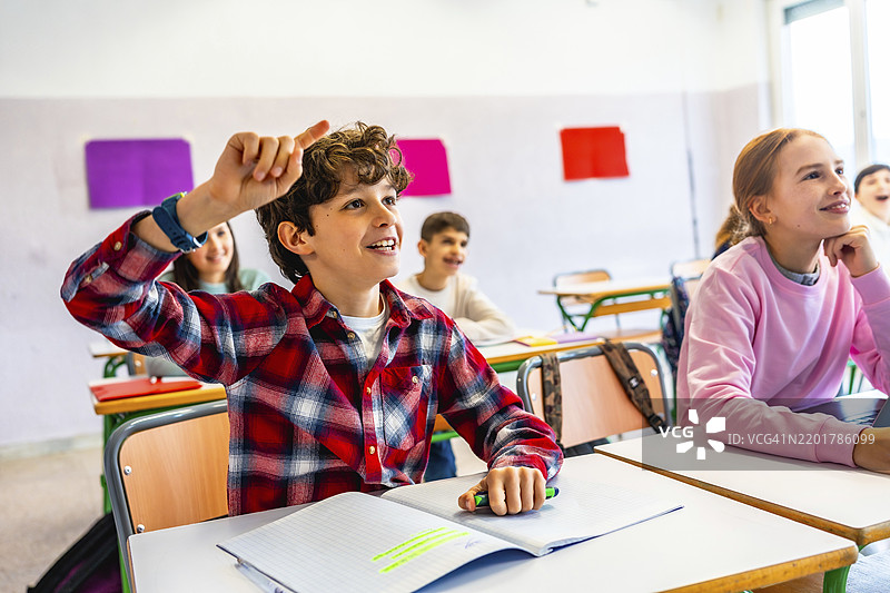小学学生在课堂上举手回答问题，表现出渴望学习和参与课堂活动的热情。图片素材