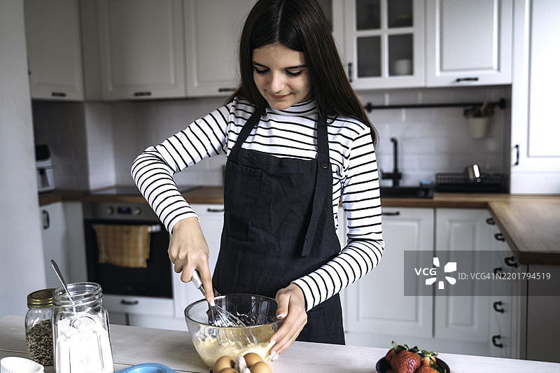 年轻女孩在温馨的厨房里搅拌面糊图片素材