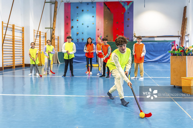 一群穿着背带的小学学生在学校体育馆里上体育课，玩地板曲棍球。图片素材