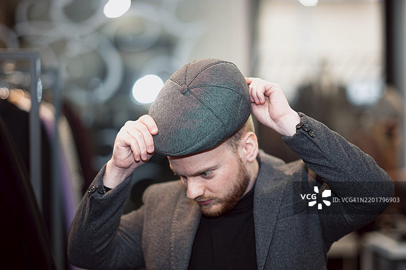穿着深色夹克的人在时尚精品店里调整头上的平顶帽图片素材