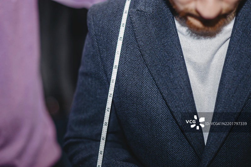 穿着海军蓝人字纹西装，肩上搭着裁缝测量带的人图片素材