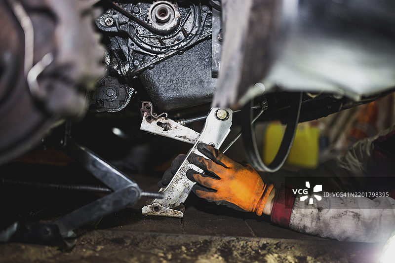 机械师在车间里用工具修理汽车发动机，戴着橙色手套。图片素材