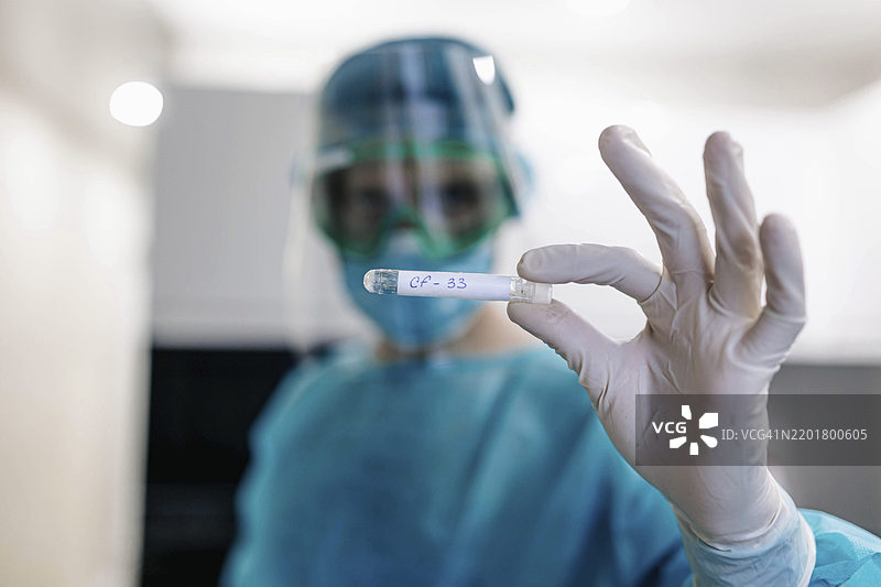 穿着防护装备的医务人员在无菌实验室中握着一个标记的试管图片素材