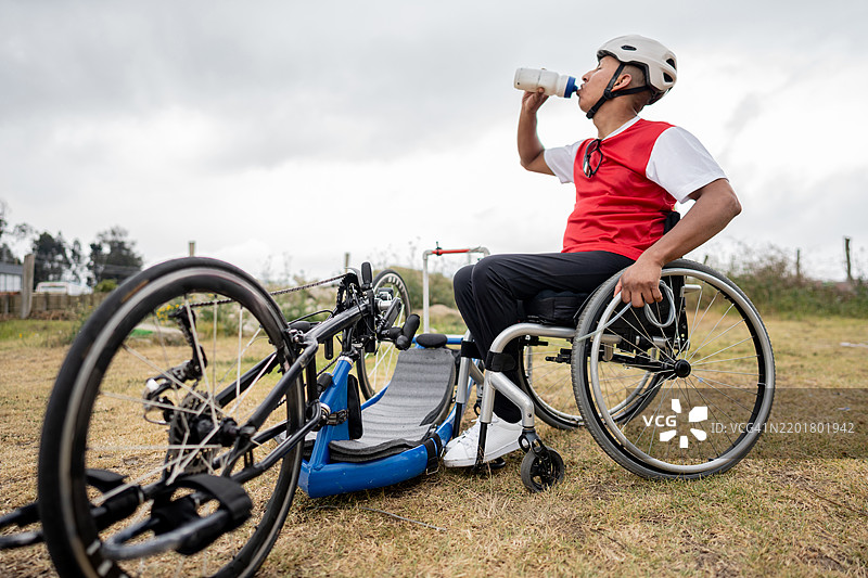 中年运动员坐在轮椅上在户外喝水图片素材