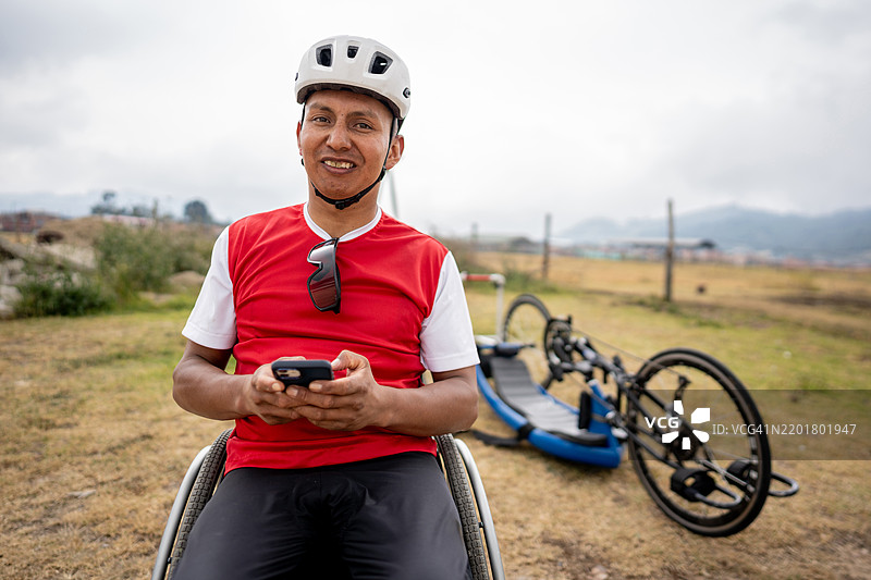 户外一位中年运动员男子坐在轮椅上使用手机的肖像图片素材
