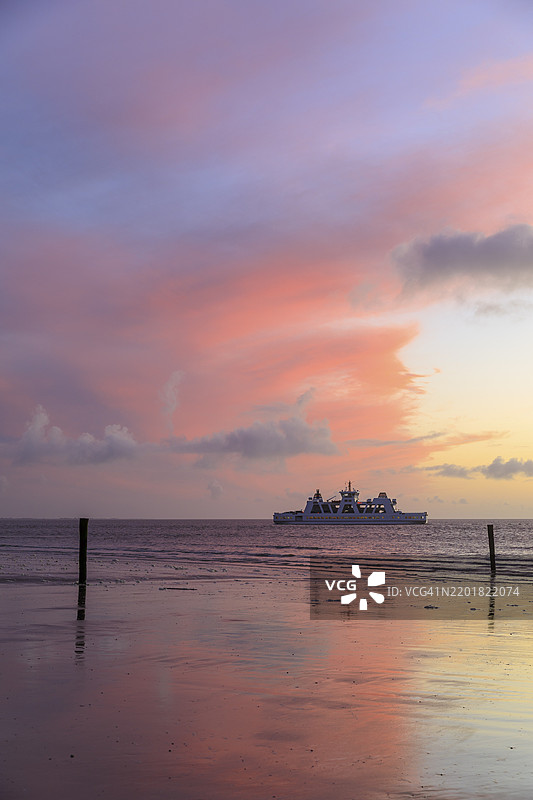 红色的晚霞映照在湿润的海滩上，渡轮，德国下萨克森州诺德奈岛的西海滩，欧洲图片素材