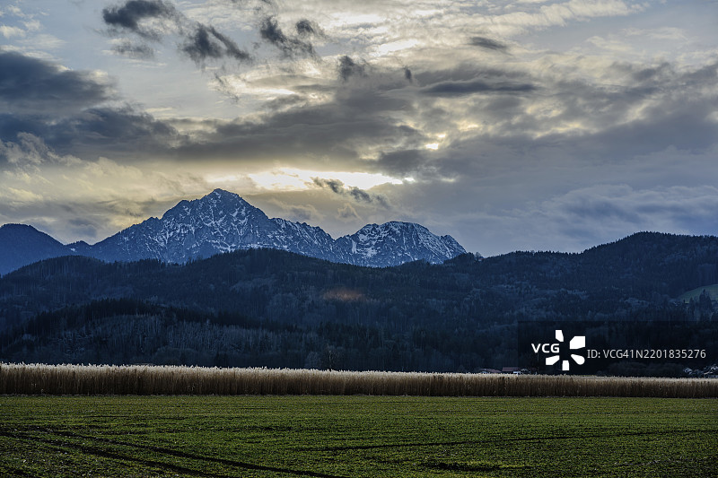 黄昏时分，前景是田野，背景是阿尔卑斯山和多云的天空，位于上巴伐利亚的艾因林。图片素材