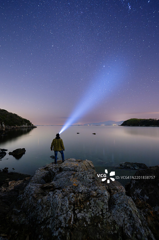 一个站在岩石上向夜空照射光线的男人图片素材