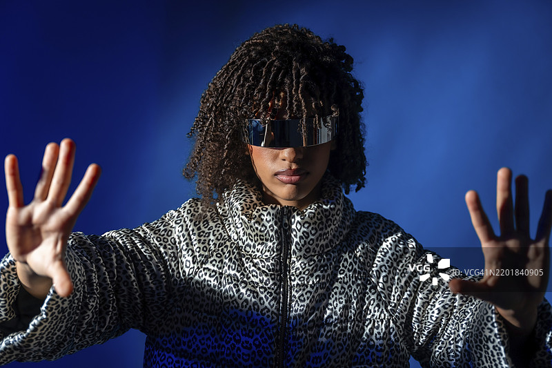 年轻女性佩戴未来感护目镜，穿着图案夹克，在蓝色背景下推动虚拟屏幕图片素材