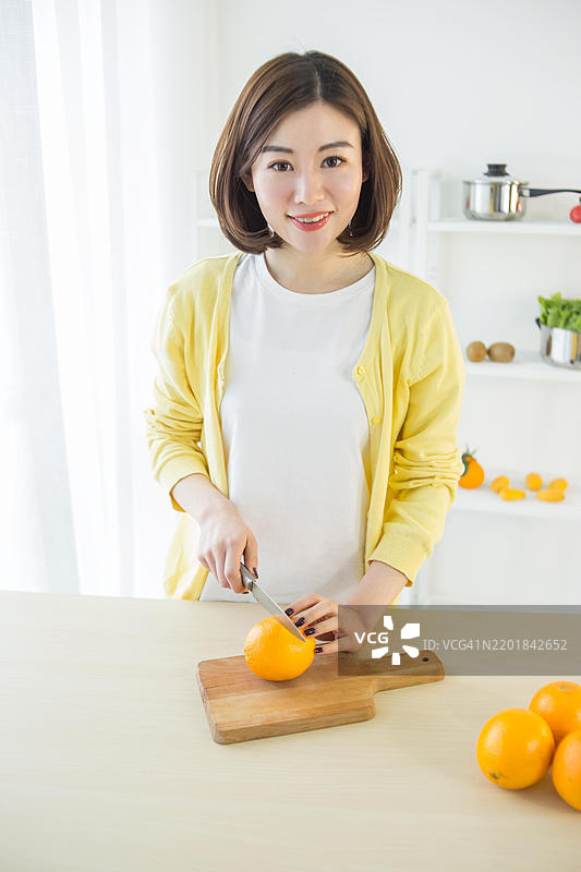 亚洲女性在厨房切橙子图片素材