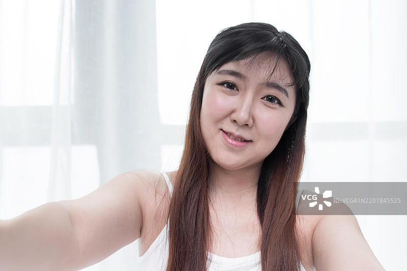 一位长发黑发的年轻女性在白色窗帘前自拍图片素材