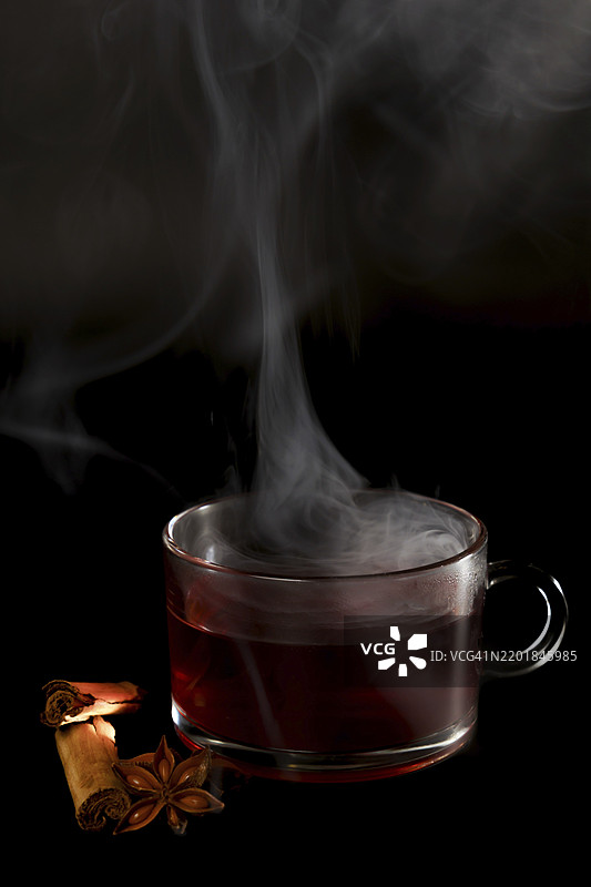 黑色背景上孤立的热茶蒸汽杯，配有八角茴香和肉桂棒，留有空白空间。图片素材