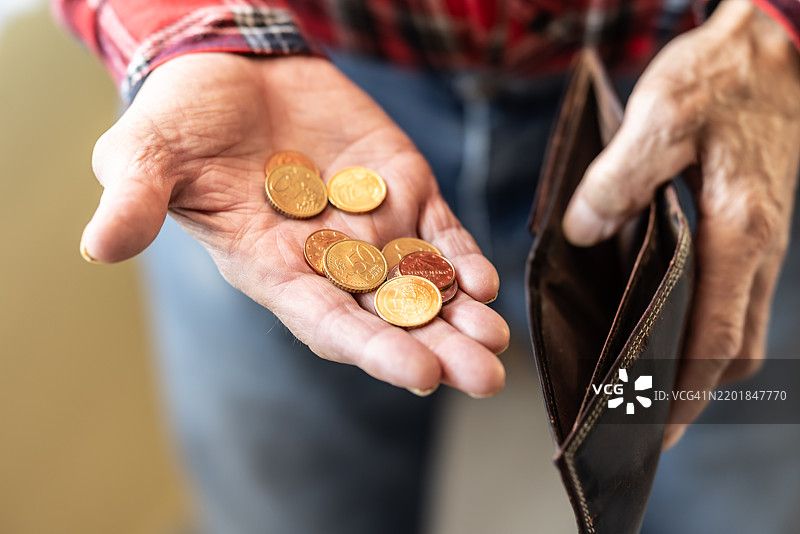 一位老年退休人员的手中拿着一个空钱包，另一只手里握着几枚硬币。图片素材