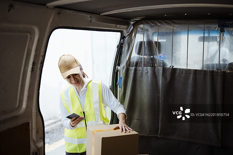 亚洲华裔快递员在送货前检查包裹。图片素材
