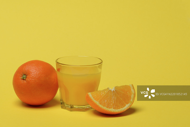 饮料杯中的橙汁和橙子，黄色背景图片素材