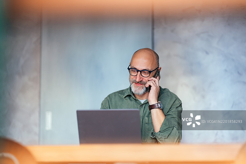成熟男性专业人士在办公室使用笔记本电脑并打电话图片素材