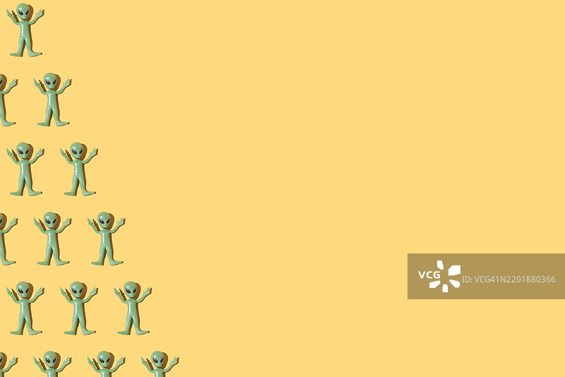 绿色外星人玩具图案，位于左侧，背景为纯黄色。外星人，虚构，科幻，恐怖，罗斯威尔，51区，外星学，飞碟，飞船图片素材