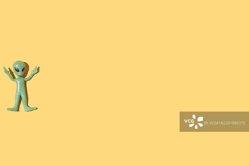 绿色外星人玩具模型，位于左侧，背景为纯黄色。外星人，虚构，科幻，恐怖，罗斯威尔，51区，飞碟学，飞碟，飞碟。图片素材