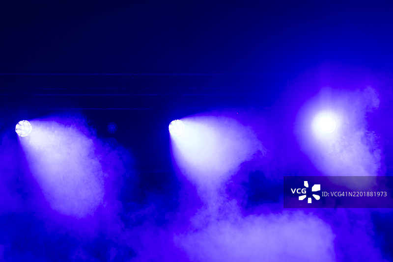 舞台上的麦克风，蓝色灯光、雾效和三束聚光灯。音乐会、表演、烟雾、派对、歌手、音乐和声音。图片素材