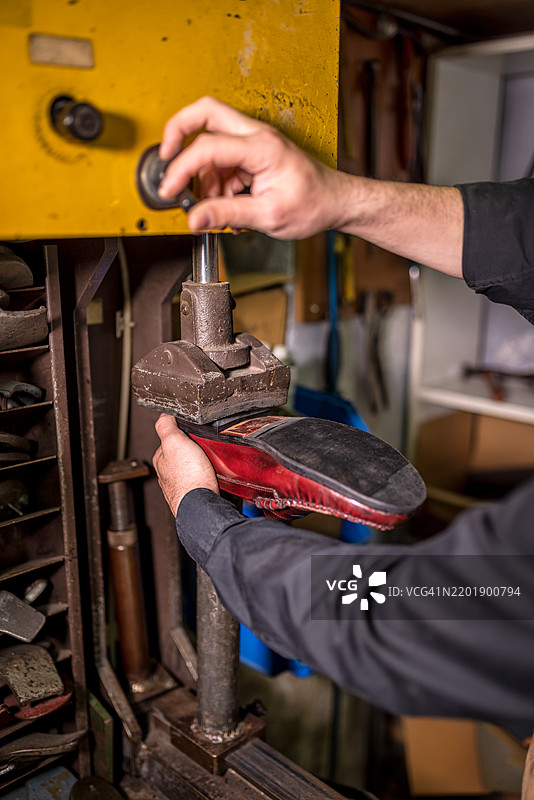 熟练的工匠正在使用复古修理机修复磨损的红色女鞋鞋底，突显精细的皮革工艺技巧。图片素材