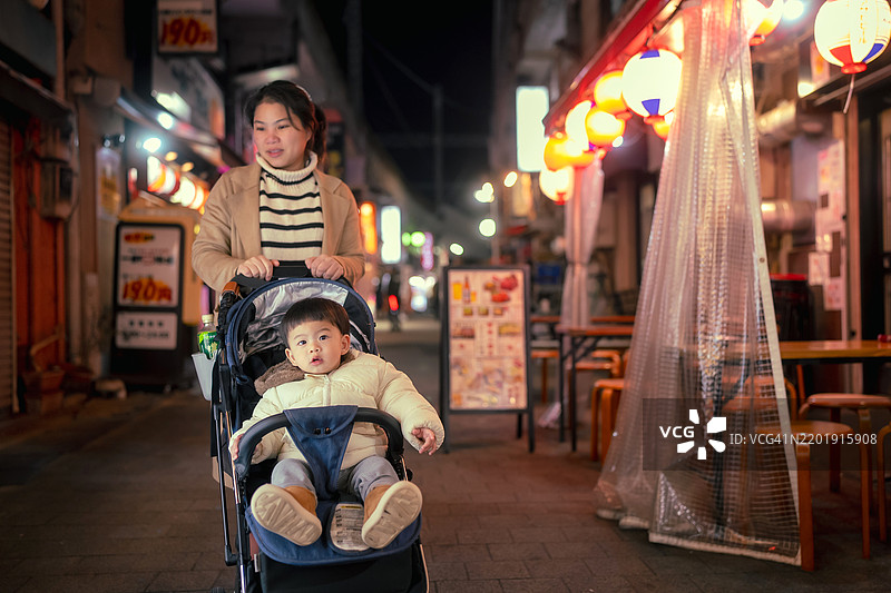 亚洲母亲在城市街道上推着婴儿推车，夜晚的日本旅行图片素材