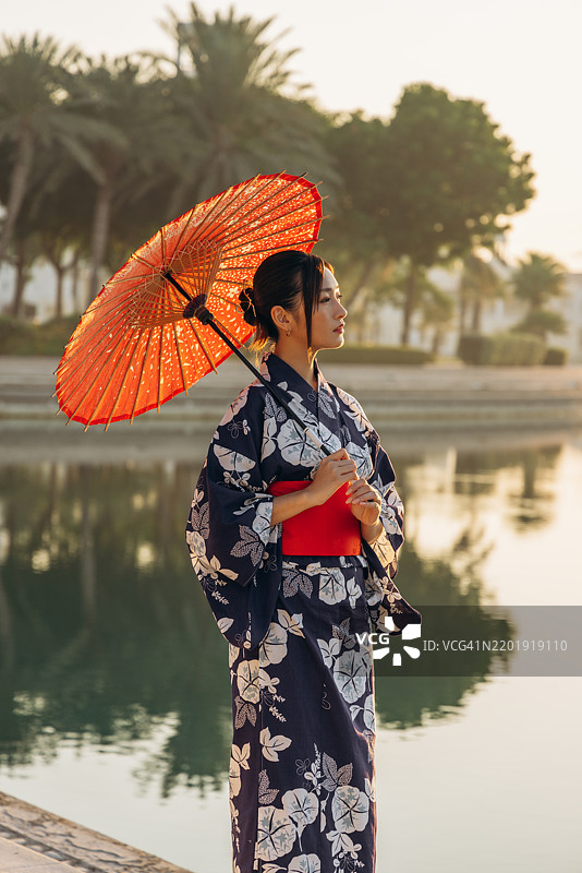 身着和服的传统女性在宁静的湖边撑着伞图片素材