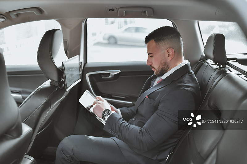 男性首席执行官坐在汽车后座上查看数字平板上的邮件图片素材