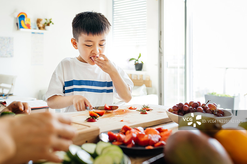 一个小男孩在厨房里帮忙时享受新鲜的草莓图片素材