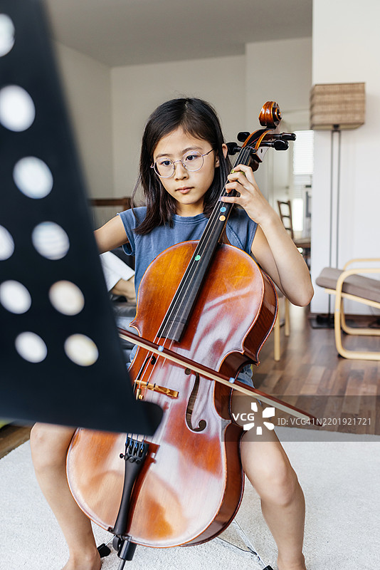 年轻女孩一边阅读乐谱一边练习大提琴图片素材