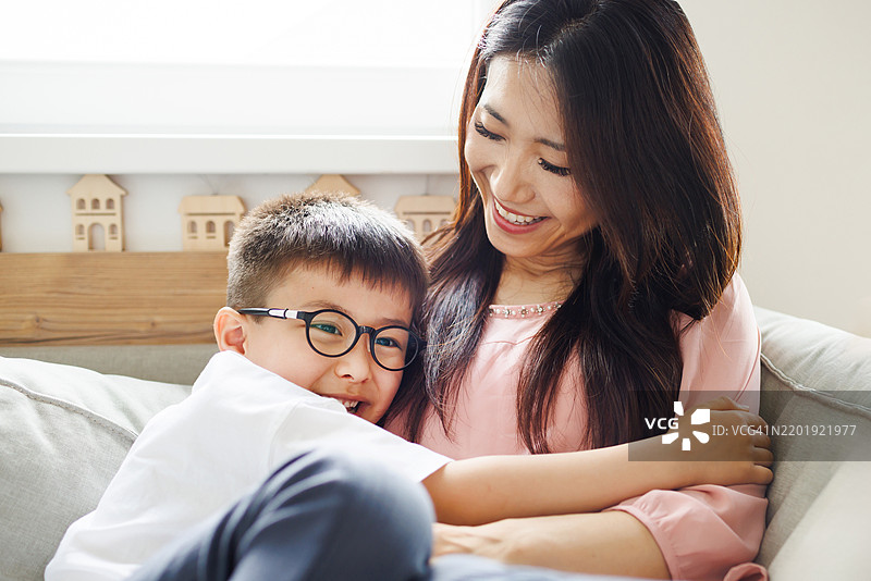 母亲和儿子在沙发上享受快乐的拥抱，笑声不断图片素材
