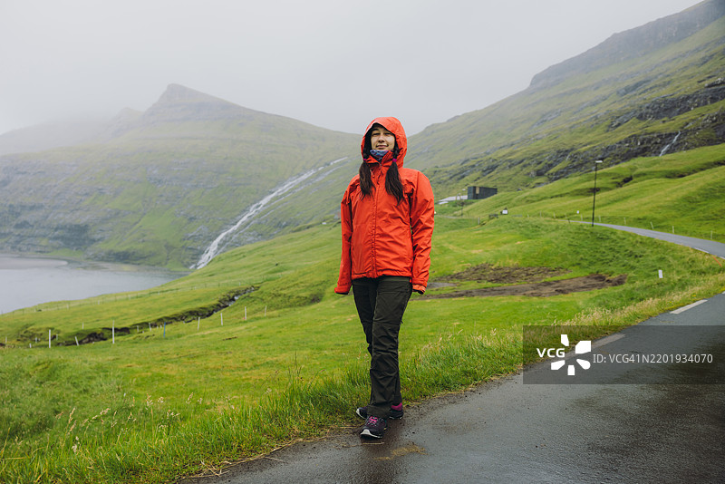 穿着红色夹克的活力女性在法罗群岛的山中探索壮丽的村庄图片素材