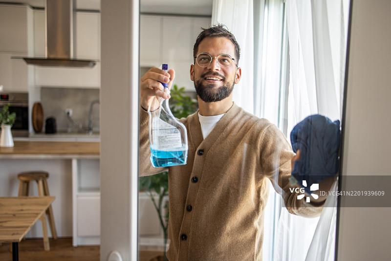 微笑的男人在他现代公寓里清洁窗户图片素材