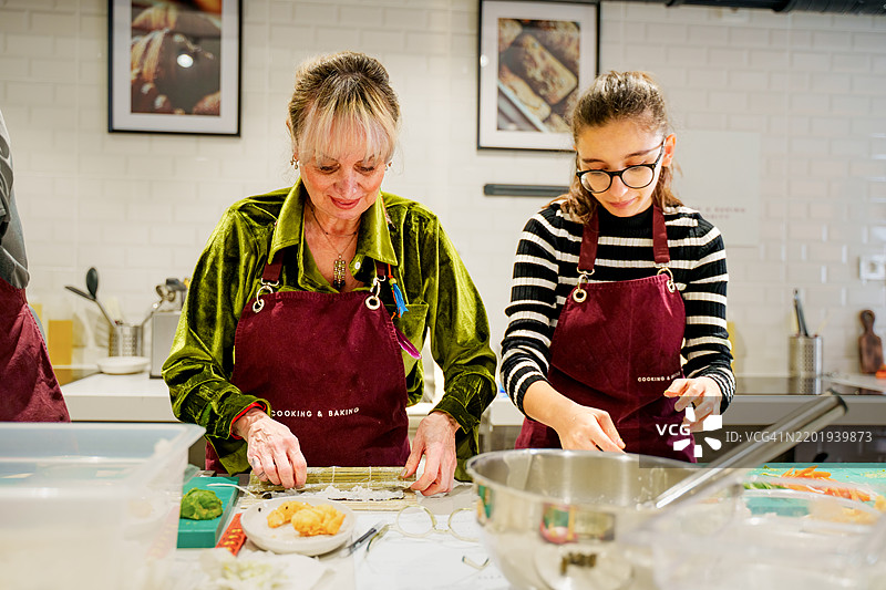 穿围裙的母女在动手烹饪课上小心翼翼地准备寿司卷。图片素材