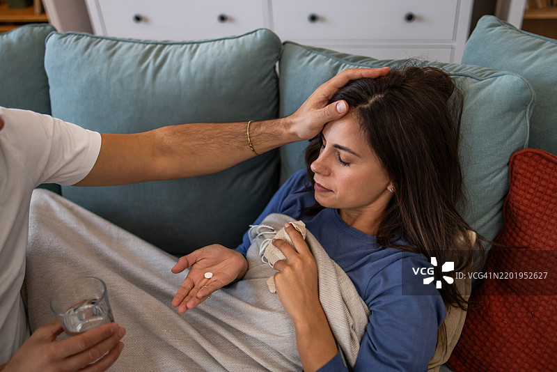 男人在给妻子测量体温并递药给她图片素材