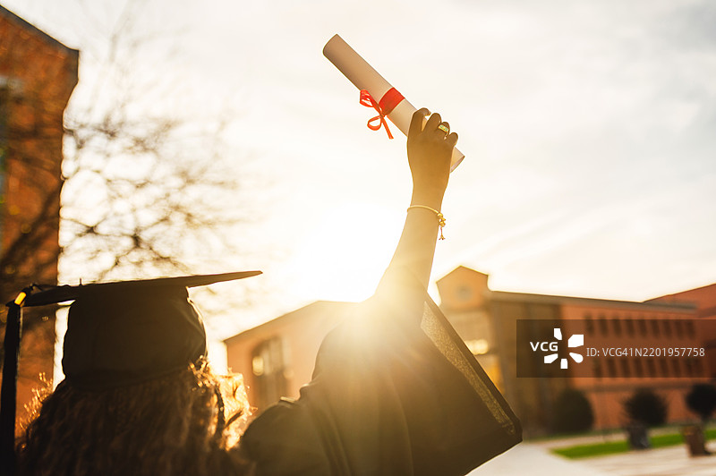 毕业生在大学校园的毕业典礼上举起她的文凭图片素材