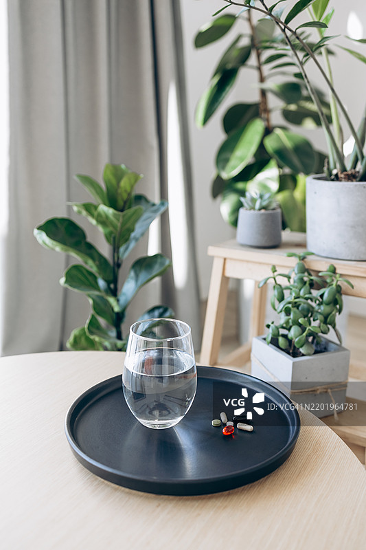 每日补充剂和水分。一杯水和各种维生素及补充剂整齐地摆放在黑色托盘上。健康、日常生活和自我护理的概念。图片素材