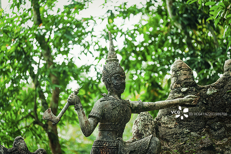 一座古老的石雕手持斧头，周围环绕着郁郁葱葱的绿植，雕像，纪念碑，塔尼姆魔法花园，纳穆昂乡，丛林，绿色，泰国，苏梅岛，亚洲图片素材