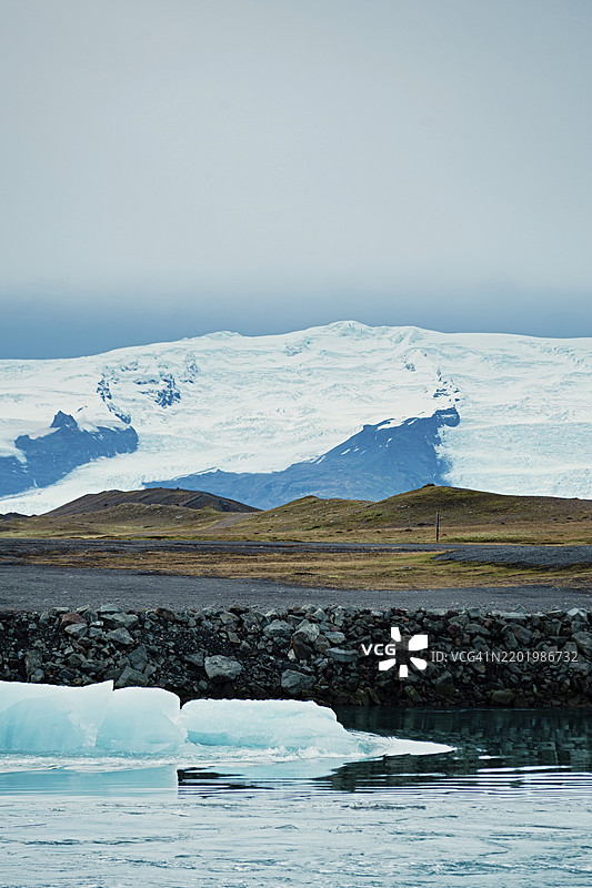 雪山和宁静的湖泊，漂浮的冰山在阴云密布的天空下，冰山，冰川，雪，冰岩，冰钻，冰川泻湖，自然，雪，钻石海滩，冰岛，欧洲图片素材