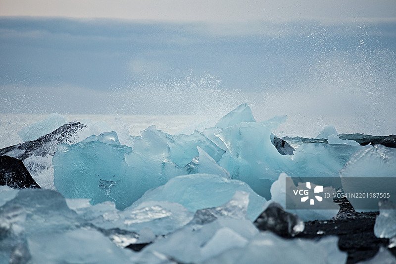巨浪拍打着巨大的冰山,场景极为壮观,广阔的冰冷景象中有冰川和崎岖的山脉,展现出宁静而寒冷的氛围,冰山,冰川,雪,冰岩,冰钻,冰川泻湖,自然,雪,钻石海滩,冰岛图片素材