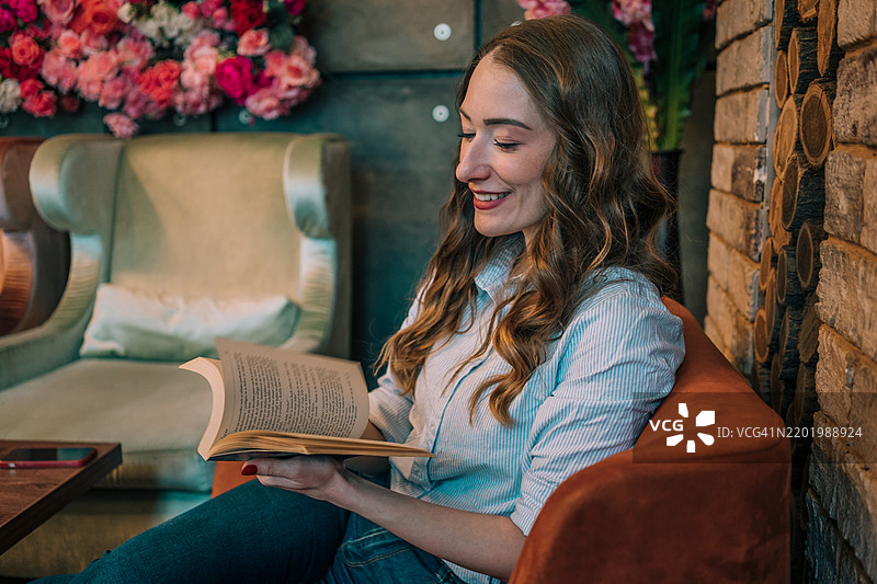 一位美丽的女性在咖啡馆温馨的氛围中放松，品尝咖啡，享受一本好书。图片素材