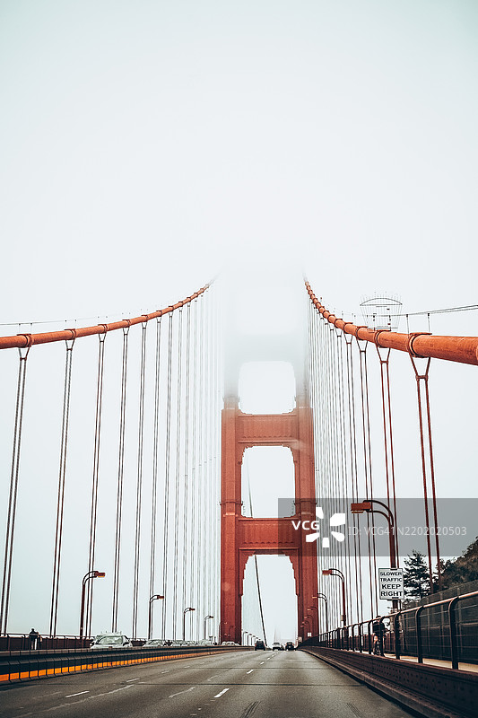 金门大桥在雾气弥漫的旧金山 - 标志性地标和旅游目的地。低角度视图显示金门大桥部分被浓雾笼罩。红色悬索与朦胧的白色天空形成鲜明对比。图片素材