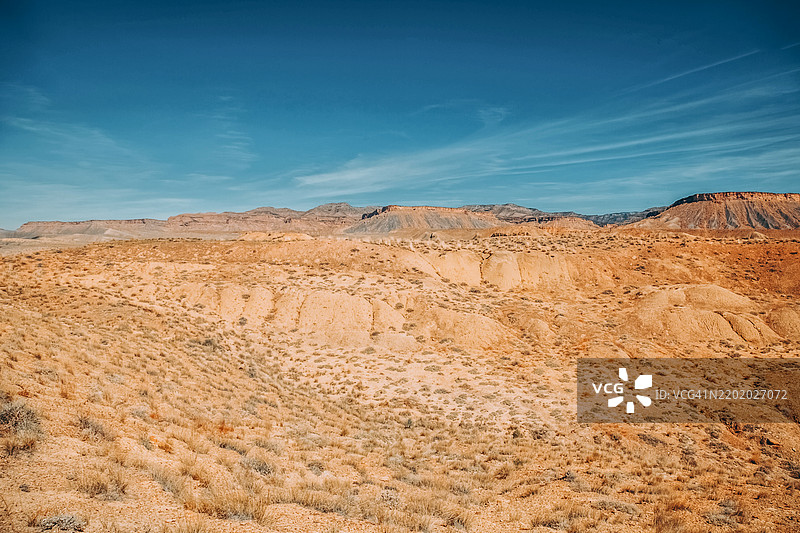 壮丽的沙漠景观在晴朗的蓝天下，干旱的山丘和广阔的地平线交相辉映。金色的沙丘延伸至地平线，干燥的岩石地形与清澈的蓝天形成鲜明对比。图片素材